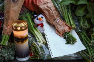 A snowman plush toy, a candle and a message are placed among flowers at a makeshift memorial near the Le Constellation bar